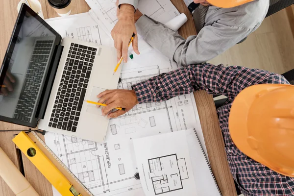 Equipo de obra revisando planos sobre la mesa con un portátil.